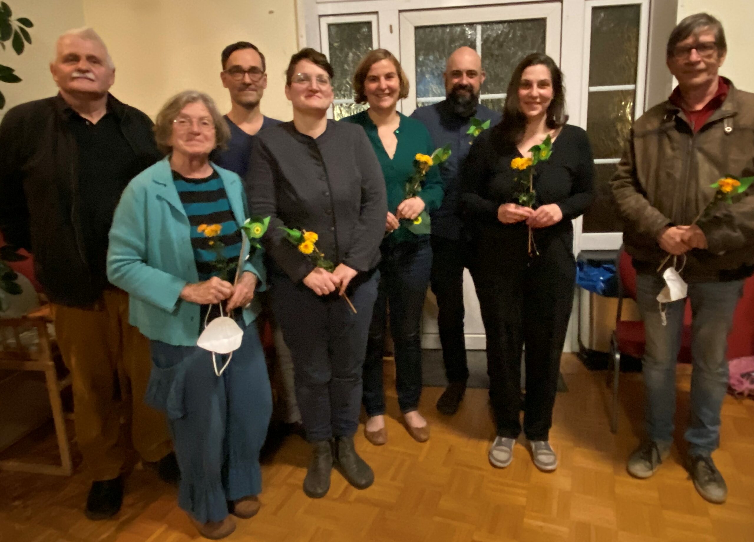 Es befinden sich acht Personen auf dem Foto. Alle schauen in die Kamera und halten eine Blume und eine Windmühle in der Hand.